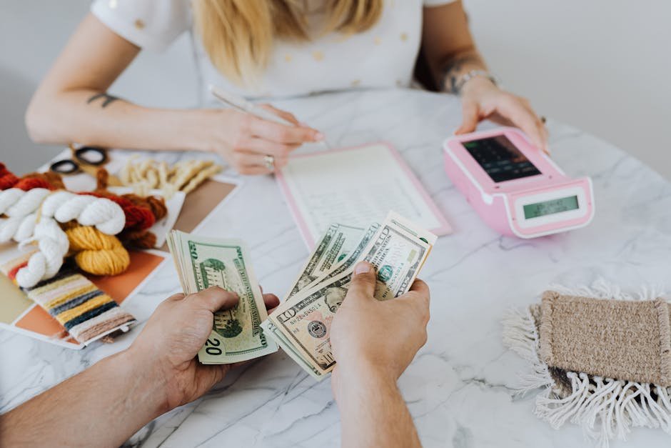 Hands exchanging cash with various denominations on a table, alongside a notebook and a pink payment device, illustrating financial planning for orthodontic treatment payments.